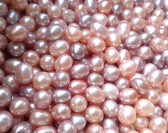 May include: A close-up view of a large quantity of oval-shaped pearls in shades of pink and purple.