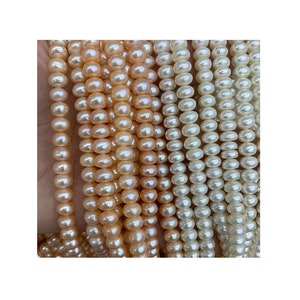 Pode incluir: Um fio de pérolas de água doce de cor branca e pêssego. As pérolas são redondas e lisas, e são enfiadas em um fio branco.