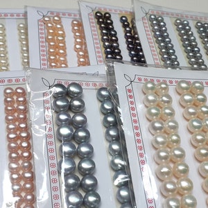 Puede incluir: Surtido de hileras de perlas en varios colores, incluyendo blanco, rosa, gris y negro. Las perlas se muestran en tarjetas con un borde decorativo.