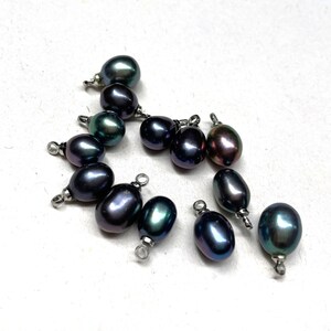 May include: A group of 11 dark green and black pearl beads with silver jump rings. The pearls are oval shaped and have a slight iridescent sheen.