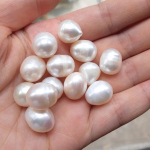 Peut inclure: Une collection de perles baroques blanches de différentes tailles et formes, présentées dans une main.