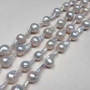 May include: A strand of white baroque pearls with an iridescent sheen. The pearls are strung on a clear thread and are arranged in a staggered pattern.