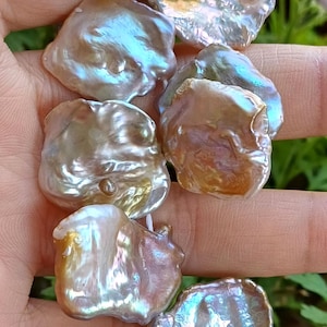 Puede incluir: Una hebra de perlas barrocas iridiscentes con una variedad de formas y tamaños. Las perlas son una mezcla de tonos blancos, dorados y rosados.