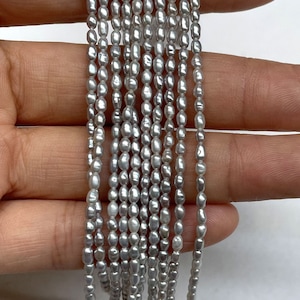 May include: A strand of 10 silver-grey freshwater pearls, each pearl is oval shaped and has a slightly irregular surface. The pearls are strung on a thin thread and are approximately 5mm in diameter.