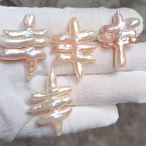 Może przedstawiać: Cztery nieregularne perły w kolorze złamanej bieli i różu są prezentowane na białym tle. Perły mają unikalny, warstwowy design, przypominający abstrakcyjne figury. Perły są prawdopodobnie przeznaczone do tworzenia biżuterii.