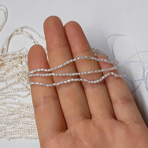 Puede incluir: Una hebra de perlas de agua dulce blancas, enhebradas en un hilo blanco. Las perlas son pequeñas e irregulares en forma, lo que les da un aspecto único y natural.