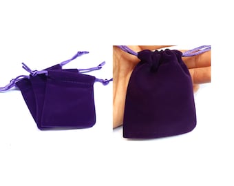 May include: Four purple velvet drawstring pouches with light purple drawstrings. The pouches are folded and stacked on a white surface.