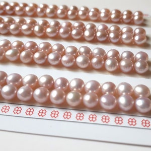 Può includere: Primo piano di una fila di perle rosa disposte a griglia su una superficie bianca. Le perle sono lisce e rotonde, e hanno una leggera lucentezza iridescente.