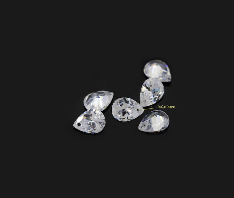 May include: Six clear pear-shaped crystals with a hole at the top. The crystals are arranged in a semi-circle on a black background.