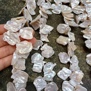 Puede incluir: Una hebra de perlas de agua dulce barrocas blancas con un brillo iridiscente. Las perlas son de forma y tamaño irregulares, y están enhebradas en un hilo blanco.