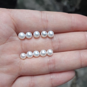 May include: A collection of ten white pearls of varying sizes, arranged in two rows on a hand.