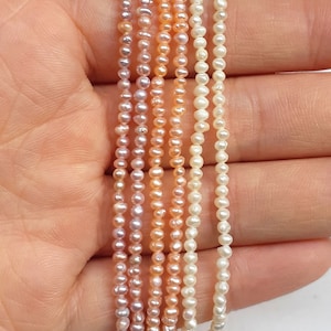 May include: A strand of freshwater pearls in various shades of pink, peach, and white. The pearls are strung on a thin thread and are approximately 3mm in diameter.