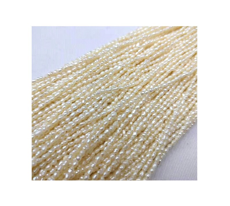 May include: A strand of off-white freshwater pearls, each pearl is a slightly irregular oval shape. The pearls are strung on a thin thread and are ready to be used for jewelry making.