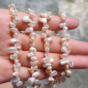 以下が含まれることがあります： 白のバロックパールが、不規則な形とサイズで、白い糸に繋がっています。パールは、わずかに虹色に輝いています。