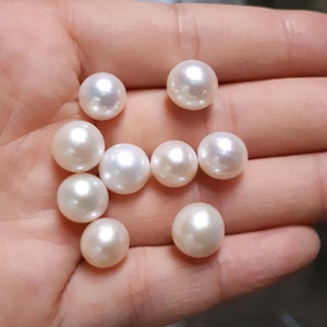 May include: A collection of white round pearls in various sizes, displayed on a hand.