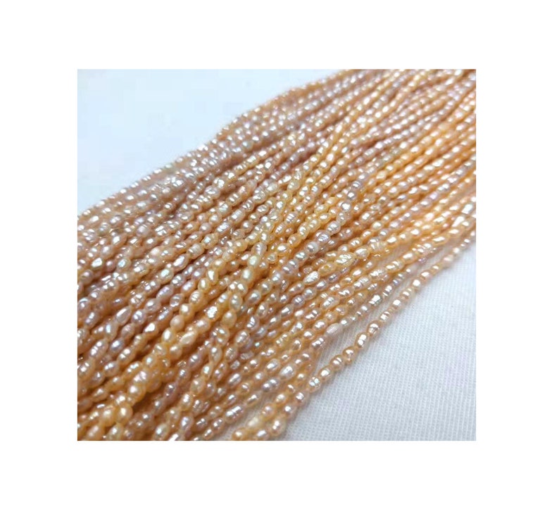 May include: A strand of small, irregular, off-white and peach-colored freshwater pearls. The pearls are strung on a thin thread and are approximately 3-4 mm in size.