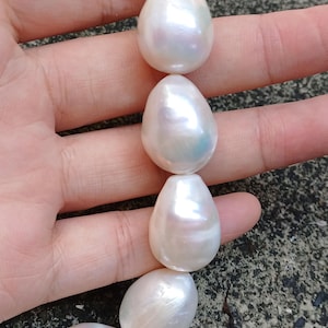 May include: A strand of large, white, baroque pearls. The pearls are strung on a clear thread and are arranged in a loose, flowing pattern.