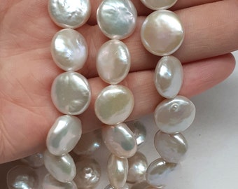 May include: A strand of white freshwater pearls with a round, flat shape. The pearls are strung on a white thread and are approximately 10mm in diameter.