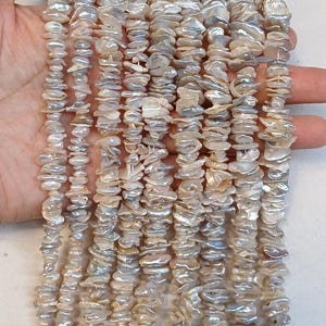 May include: A strand of white and iridescent freshwater pearl beads. The beads are irregular in shape and have a natural, organic look. The strand is approximately 18 inches long.