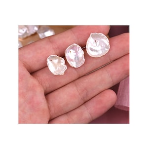 May include: Three white, irregular shaped, pearl shell pendants with a hole drilled through the top. The shells are iridescent and have a natural, organic shape.