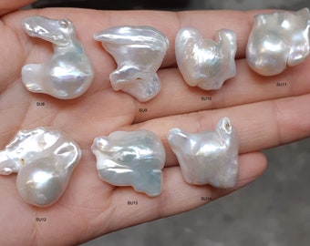 Pode incluir: Uma coleção de oito pérolas barrocas brancas com formas irregulares e superfícies iridescentes. As pérolas são etiquetadas com os números SU8 a SU14.