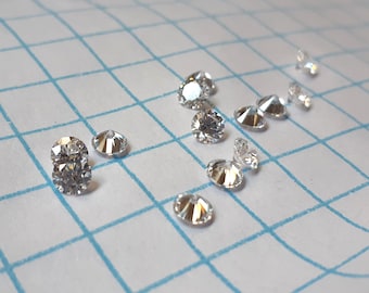 May include: A collection of clear, round, faceted gemstones on a white gridded surface. The gemstones are various sizes and shapes.