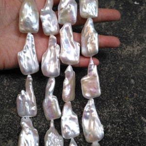 Op de afbeelding: Een streng witte barokparels met een iriserende glans. De parels zijn onregelmatig van vorm en hebben een natuurlijke, organische uitstraling.