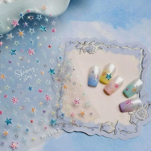 May include: Nail art stickers featuring a variety of colourful star designs. The sheet displays stars of different sizes and colours, some with polka dots. The text "Shining Star" is visible. Several nails are decorated with star stickers, showcasing different colour gradients.