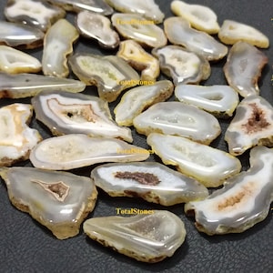 May include: A collection of agate slices in various shapes and sizes. The agate slices are translucent and have a white, brown, and yellow colour scheme. The agate slices are arranged on a black surface.