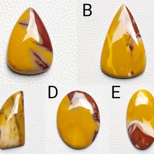 Op de afbeelding: Vijf gepolijste gele, rode en witte edelsteencabochons in verschillende vormen, waaronder druppel, ovaal en onregelmatige vormen. De stenen zijn gerangschikt in een rasterpatroon op een witte achtergrond.