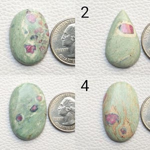 Puede incluir: Cuatro piedras preciosas con una moneda de veinticinco centavos para comparar el tamaño. Las piedras preciosas son de forma ovalada y de lágrima, con un color base verde claro e inclusiones rosas y rojas. Las piedras tienen un acabado pulido.