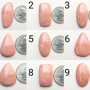 Puede incluir: Nueve cabujones de piedras preciosas de rodonita rosa pulida en varias formas, incluyendo ovaladas, de lágrima y rectangulares. Cada piedra se muestra junto a una moneda para comparar el tamaño. Las piedras tienen un acabado liso y brillante.