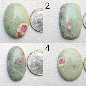May include: Four polished gemstones with a quarter coin for size comparison. The stones are oval and rectangular, with a light green base colour and patches of pink and red. The gemstones have a smooth, polished surface.