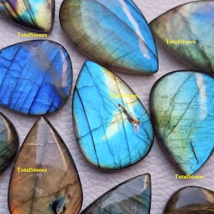 May include: A collection of labradorite gemstone cabochons in various shades of blue, green, and brown. The stones are pear-shaped and have a iridescent sheen. TotalStones is printed on several of the stones.