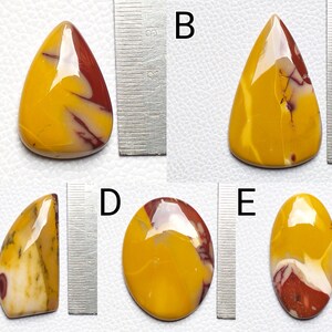 Op de afbeelding: Vijf gepolijste edelsteencabochons in verschillende vormen en maten. De stenen zijn een mix van geel, rood en wit met draaiende patronen. De stenen worden naast een liniaal getoond ter referentie van de grootte.