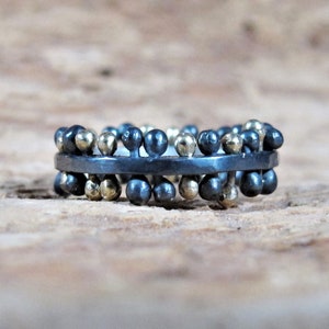 Peut inclure: Une bague noire et dorée avec une bande de petites perles rondes. Les perles sont disposées en quinconce, certaines étant dorées et d'autres noires.