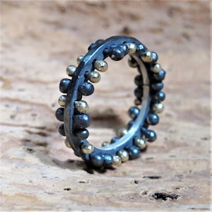 Peut inclure: Une bague noire et dorée avec une bande texturée et de petites perles dorées autour du bord.