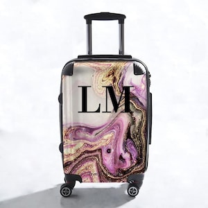 Könnte beinhalten: Ein schwarzer Trolleykoffer mit einem pinkfarbenen, goldenen und weißen Marmormuster und den Initialen "LM" in Schwarz.