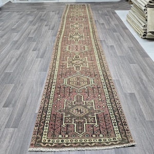 Könnte beinhalten: Ein langer, schmaler Teppich mit traditionellem persischem Design. Der Teppich hat einen roten Hintergrund mit komplizierten Mustern in Braun-, Beige- und Cremetönen. Der Teppich ist an beiden Enden gefranstet.