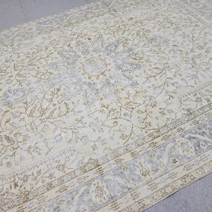 May include: Cream-colored vintage rug with an intricate floral pattern. The rug features a central medallion design with surrounding floral motifs in shades of beige, brown, and blue. The border has a detailed pattern. The rug is rectangular.