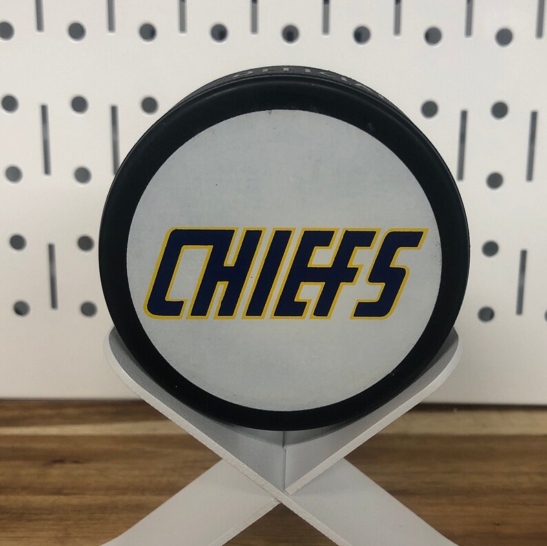 Chiefs hockey puck front side displayed on edge on a white stand that looks like crossed hockey sticks