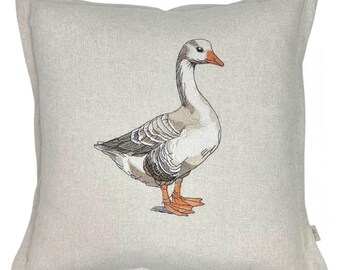 Könnte beinhalten: Ein beigefarbenes Leinenkissen mit einem gestickten Bild einer grauen Gans mit orangefarbenem Schnabel und Füßen.