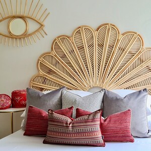 May include: A bed with a large, woven headboard in the shape of a flower. The headboard is made of natural rattan and has a light brown color. The bed is dressed with a white duvet and several pillows in shades of gray and red.