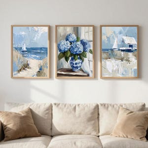 Puede incluir: Conjunto de tres láminas enmarcadas. Las obras presentan pinturas impresionistas de una escena costera con un velero, un jarrón de hortensias azules y una casa junto al mar. La paleta de colores incluye tonos de azul, beige y blanco.