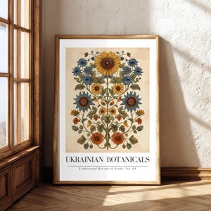 May include: Framed art print featuring a symmetrical botanical design with sunflowers, blue and orange flowers, and green leaves. The print is labeled "UKRAINIAN BOTANICALS" with "Traditional Botanical Study, No. 04" below. The artwork is displayed in a wooden frame.