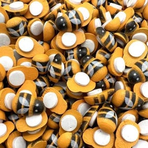 Puede incluir: Una gran colección de pequeños adornos de madera con forma de abeja. Cada pieza presenta un cuerpo a rayas amarillas y negras con un acabado liso y redondeado, y un soporte adhesivo blanco circular y plano en la parte inferior.