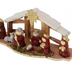 Op de afbeelding: Een rood-gouden kerststal met een houten stal, een ster en beeldjes van Maria, Jozef, baby Jezus, een herder, een schaap en drie wijzen.