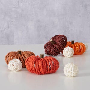 Könnte beinhalten: Vier kleine dekorative Kürbisse aus geflochtenem Papier in den Farben Orange, Braun und Rot. Die Kürbisse sind auf einer weißen Oberfläche angeordnet, mit drei weißen Kugeln aus geflochtenem Papier.