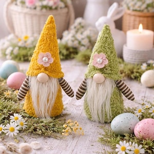 Può includere: Due gnomi pasquali con cappelli a cono gialli e verdi, lunghe barbe bianche e braccia a righe. Ogni gnomo ha un fiore rosa con un centro di perla. Gli gnomi sono circondati da muschio, margherite e uova di Pasqua pastello.