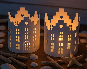 May include: Two white paper candle holders shaped like a castle with cut-out windows and hearts. The candle holders are lit and casting a warm glow.